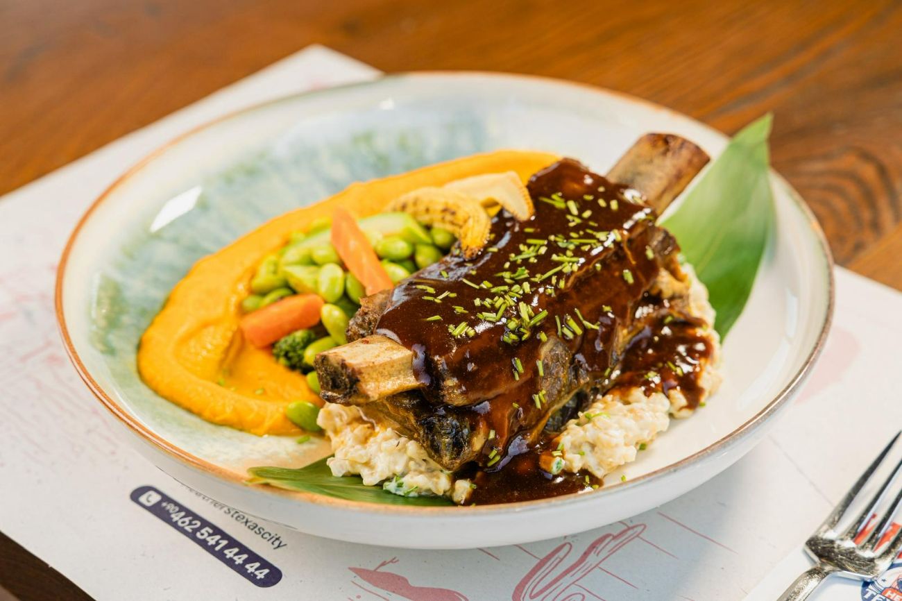 BEEF WESTERN ASADO - Ağır Ateşte 12 Saat Boyunca Pişmiş 380 Gr  Dana Kaburga, Frenk Soğanlı Buğday Risotto Yatağında; Demi Glace Sos, İpeksi Havuç Püresi, Soya Fasulyesi, Izgara Beybi Mısır ve Sote Mevsim Sebzeleri Eşliğinde