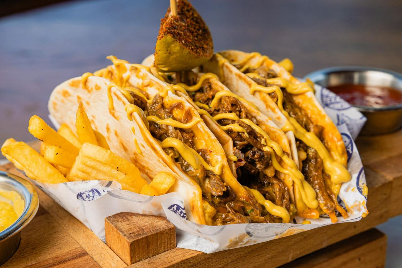 TİFTİK KABURGA TACO - Soft Taco Tortilla İçinde, Ağır Ateşte Pişmiş Tiftik Kaburga Parçaları, Cheddar Peyniri, Crispy Root Slaw, Mor Soğan, Maydonoz, Gewürzgürken Turşu, Baharatlı Patates Kombinasyonu Salsa Ve Guacomale Sosları Eşliğinde…