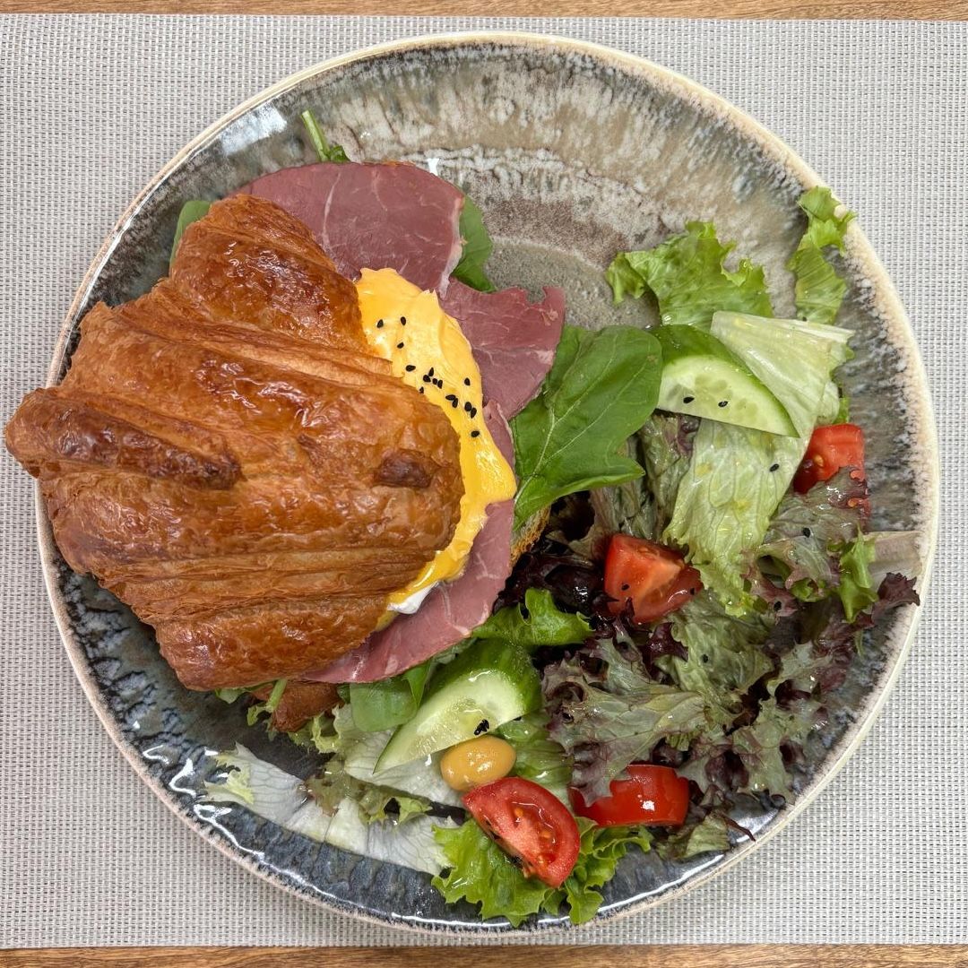 Croissant Sandwich with Poached Egg - Smoked meat, poached egg, arugula, Hollandaise sauce, nigella seeds; served with salad.