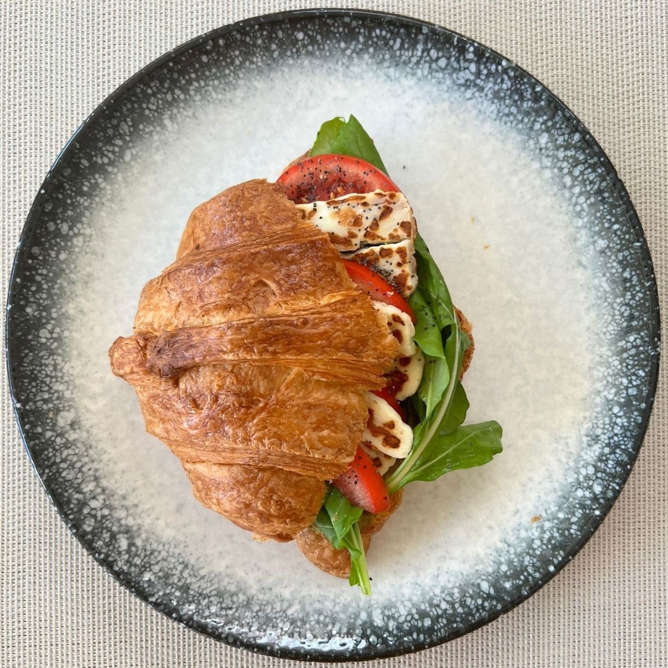 Halloumi Sandwich Croissant - Halloumi cheese, pesto sauce, tomatoes, arugula, poppy seeds; served with salad.