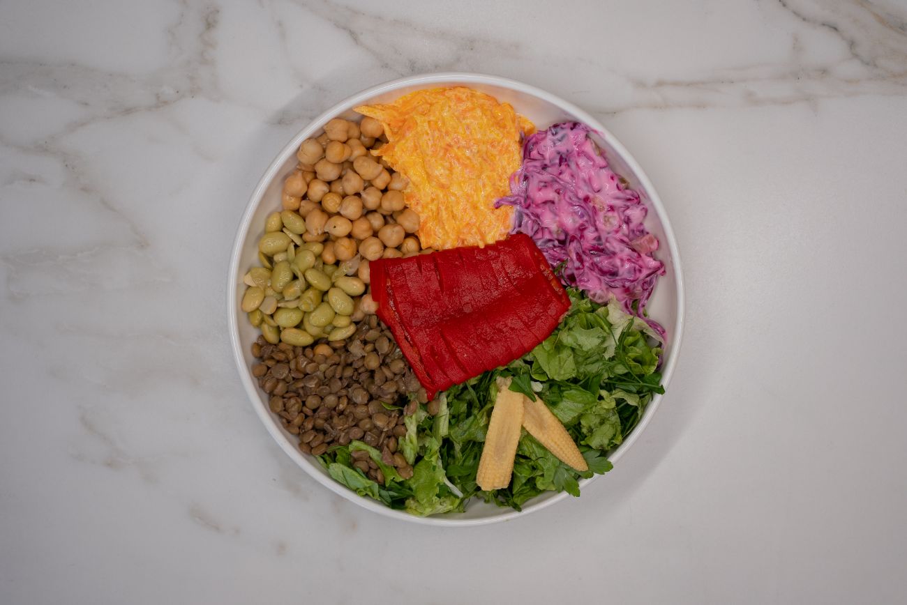 Sebzeli Bakliyat Bowl - Haşlanmış nohut, yeşil mercimek, iç bakla, közlenmiş kırmızı biber, baby mısır, havuçlu yoğurtlu meze ve mor lahana salatası taptaze yeşilliklerle buluşuyor. Protein ve lif açısından zengin bu rengarenk bowl, hafif ama doyurucu bir öğün arayanlar için mükemmel bir seçenek!