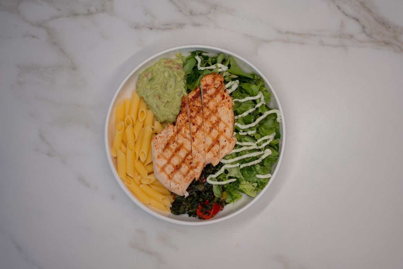 Fit Tavuk Bowl - Izgara tavuk göğsü, glütensiz penne makarna, guacamole, mevsim yeşillikleri ve kavrulmuş sebzelerle hazırlanan sağlıklı ve doyurucu bir bowl. Özel yeşil sos eşliğinde, hem hafif hem de protein açısından zengin bir lezzet!