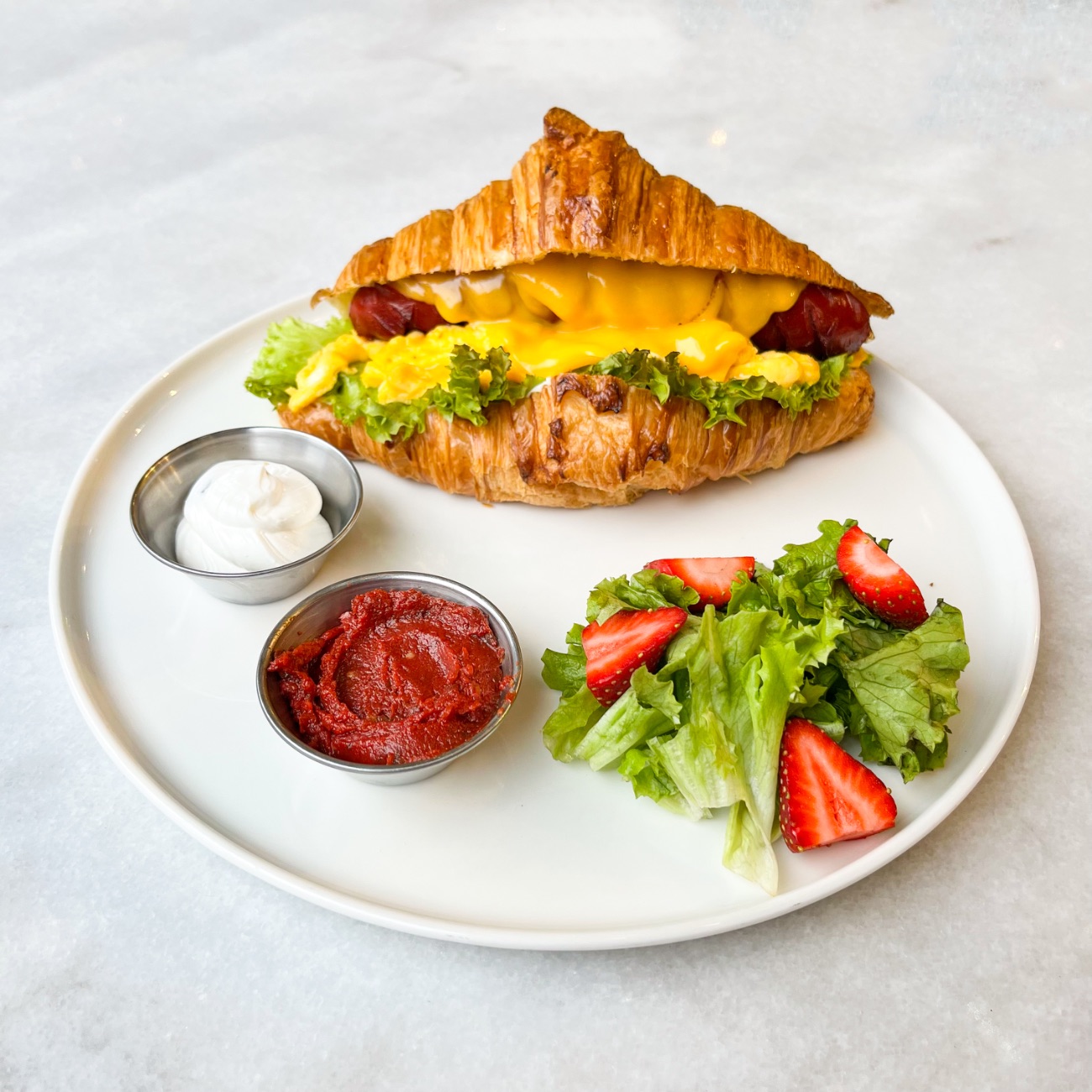 Frankfurter Sosis Kruvasan - Frankfurter Sosis, Marul, Çırpılmış Yumurta, Cheddar Peynir, Pesto Sos. Yanında Peynir Sos ve Acuka ile servis edilir.