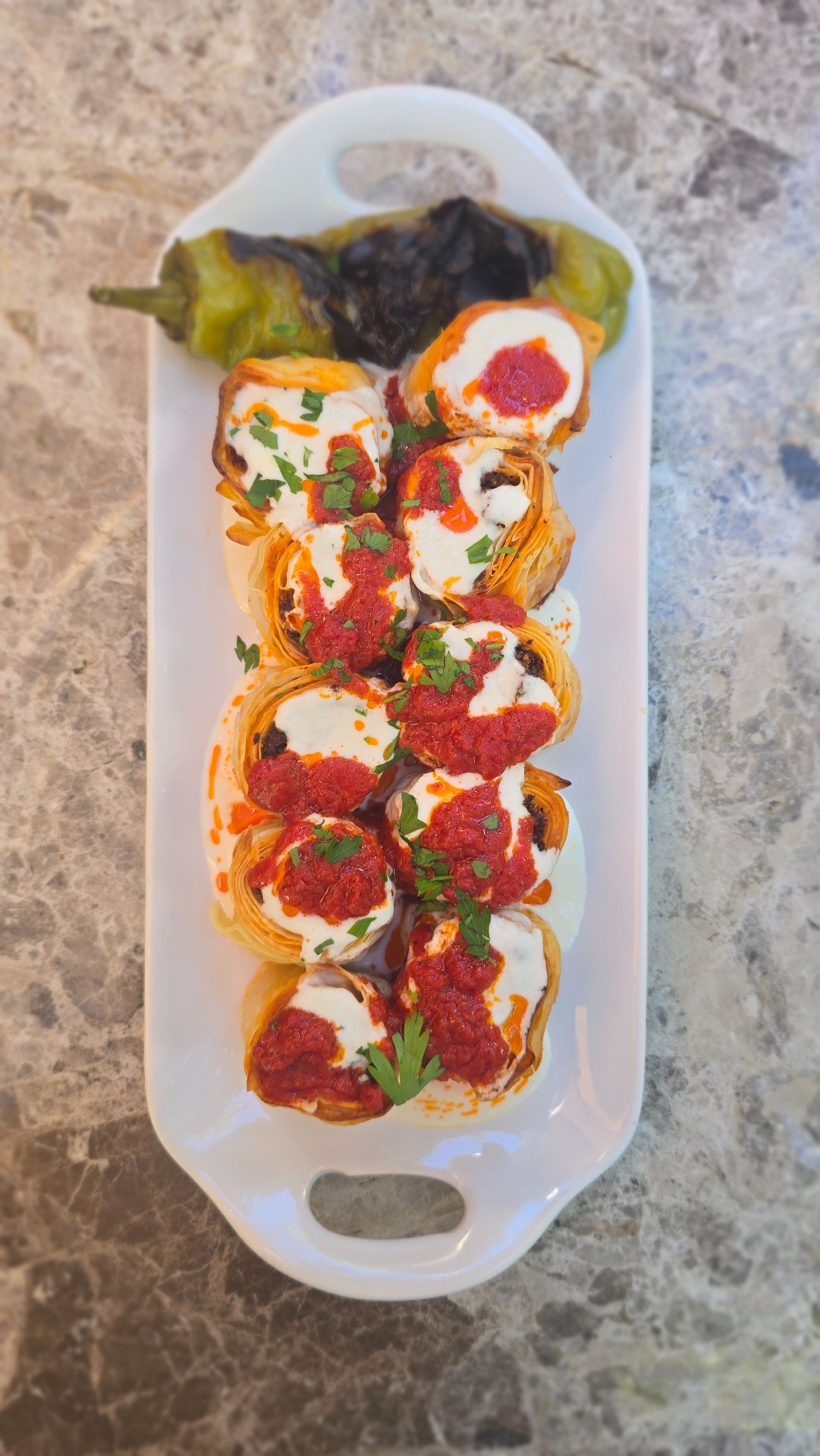 Beyti - A vegan twist on the traditional dish 'Beyti'. Soy-mince stuffed phyllo dough rolls are served with almond yoghurt and tomato sauce on top.