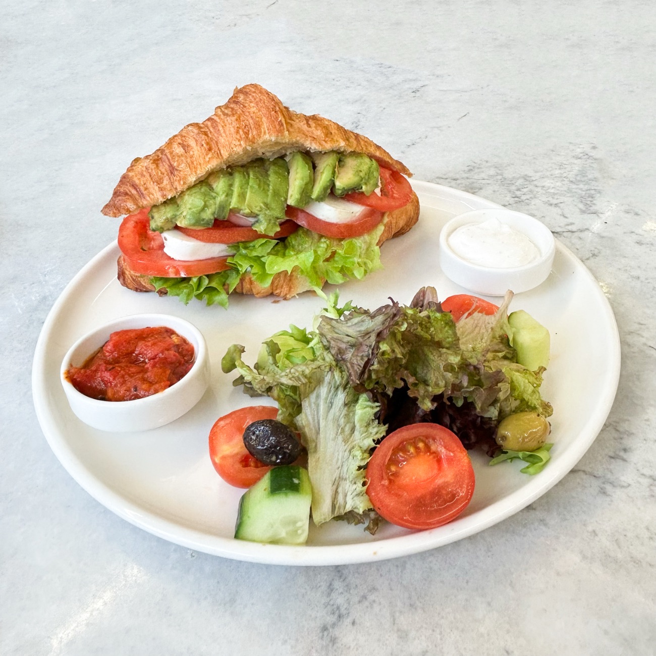 Mozzarella Caprese Kruvasan - Mozzarella Peynir, Pesto, Domates, Avocado, Kıvırcık, Peynir Sos, Akdeniz Yeşillikleri, Çeri Domates, Salatalık, 2 Çeşit Zeytin. Yanında Acuka ve Peynir Sos ile servis edilir.